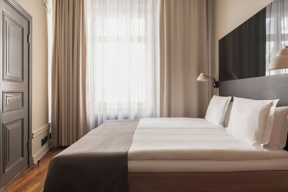 A neatly made bed with white linens, a dark headboard, and a bedside lamp.