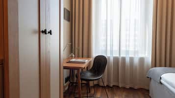 A hotel room with a wooden desk, a chair, a bed, and a window with curtains.