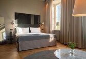 A modern hotel room with a large bed, a round marble table, and a view of the outdoors.