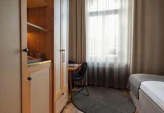 A hotel room with a bed, a desk with a chair, a wardrobe, and a window with curtains.