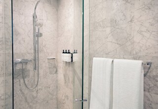 A modern bathroom with a glass-enclosed shower, marble walls, and a towel rack with two white towels.