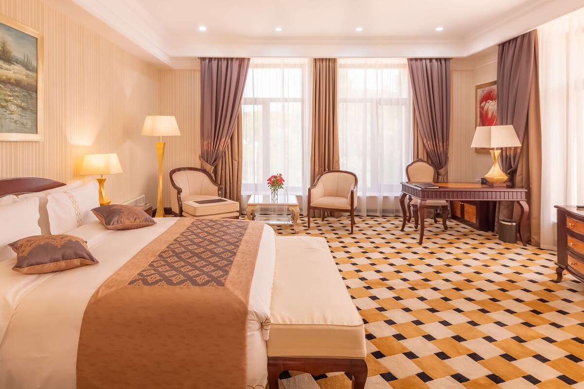 A hotel room with a large bed, a desk, a chair, a television, and a patterned floor.