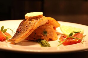 A plate with a piece of grilled fish, a slice of bread, and some vegetables.