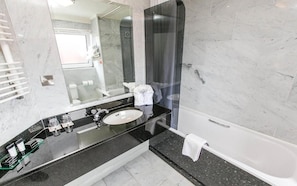 Casa de banho moderna com cabine de duche em vidro, lavatório com bancada preta e toalha branca no chão.