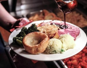 A plate with food items including a Yorkshire pudding, mashed potatoes, and a meat dish, being served.