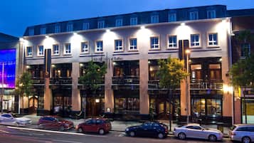 Un hôtel à plusieurs étages, doté d’une façade classique, de nombreux balcons et d’une rangée de voitures garées devant.