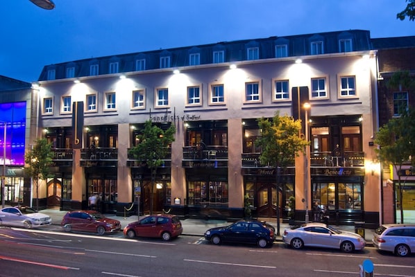 Um hotel de vários andares com fachada clássica, diversas varandas e uma fila de carros estacionados em frente.