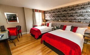 A hotel room with two beds, a desk with a chair, a desk lamp, and a patterned wall.