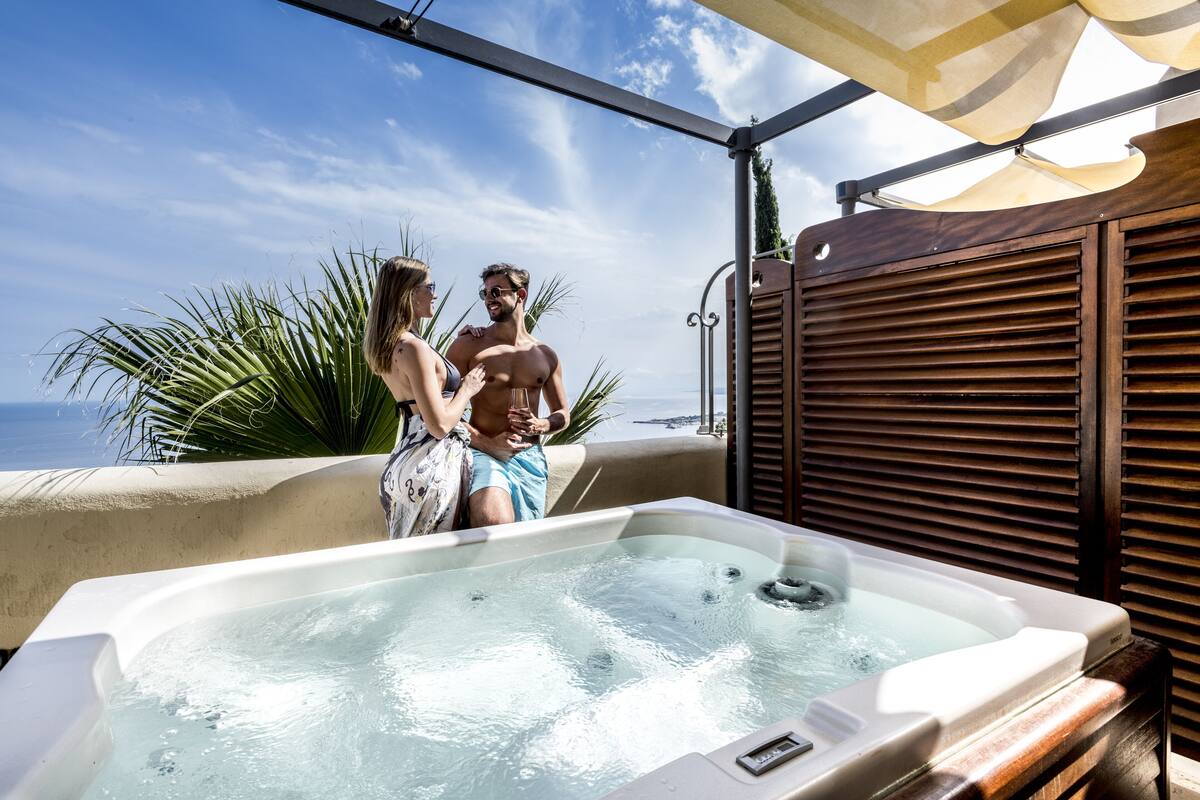 A hot tub with a view of the ocean, a wooden structure, and a palm plant.