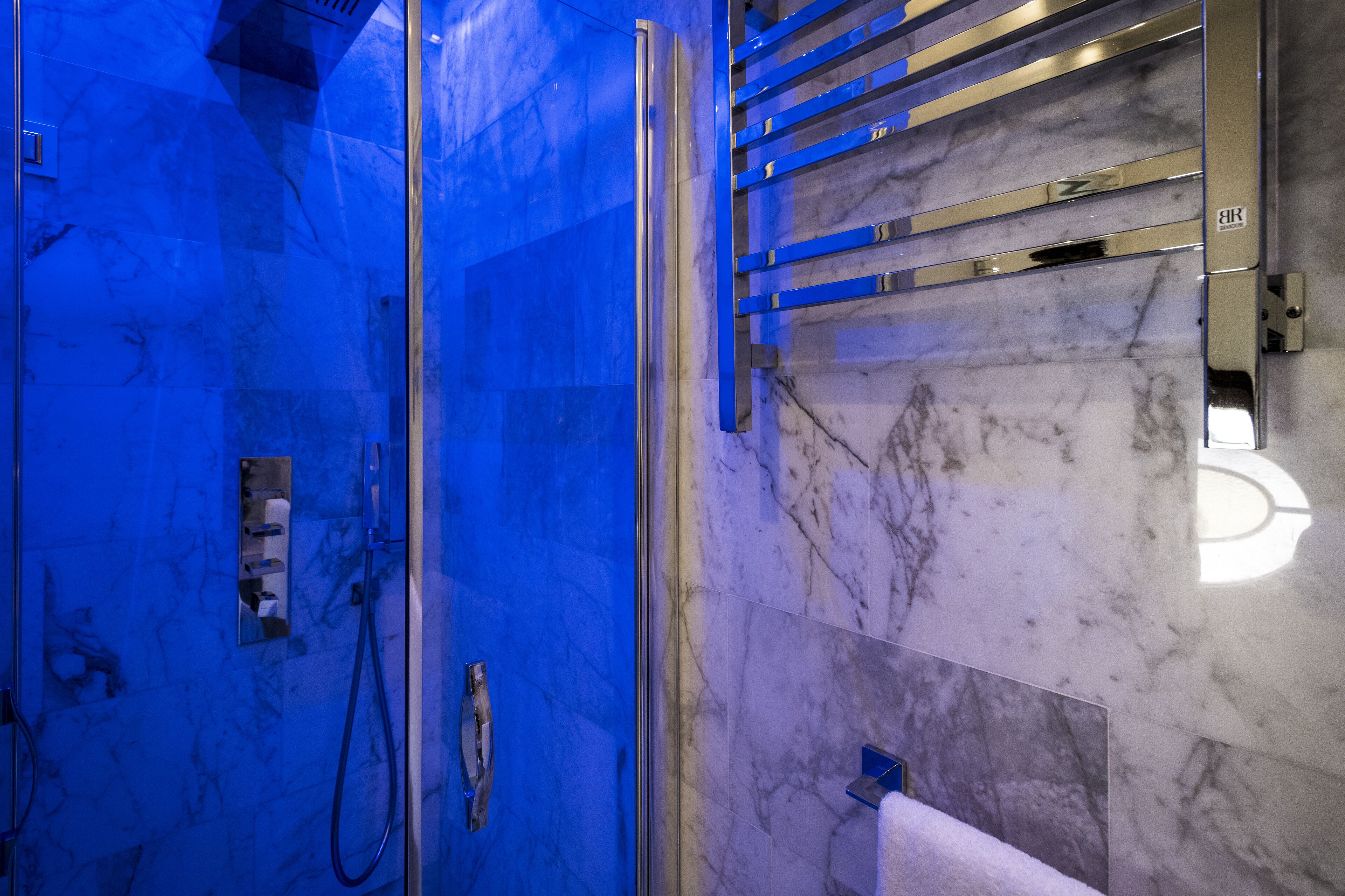 Un baño con cabina de ducha de vidrio, pared revestida de mármol y un perchero para toallas.