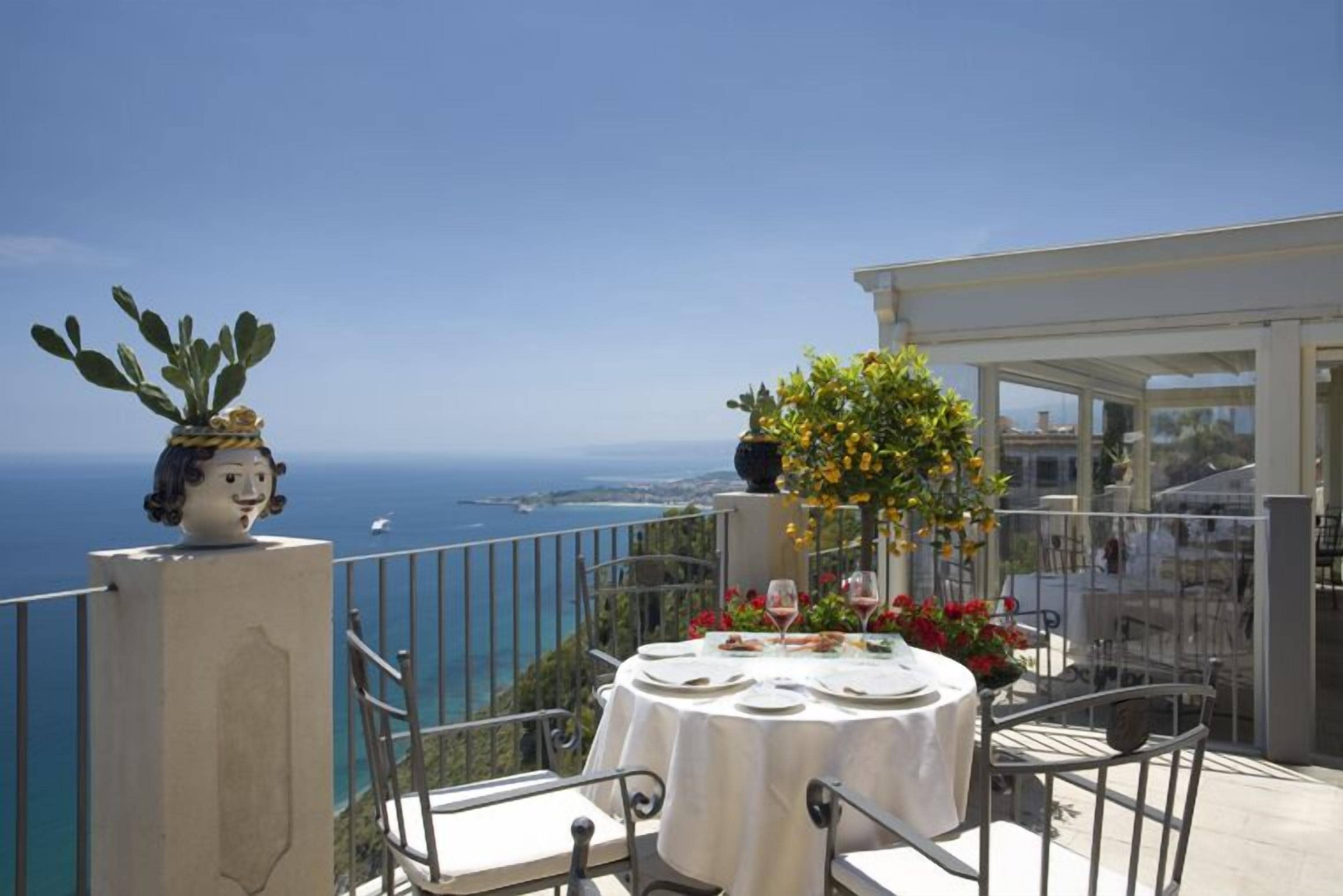 A balcony with a table set for two, overlooking a scenic coastal view.