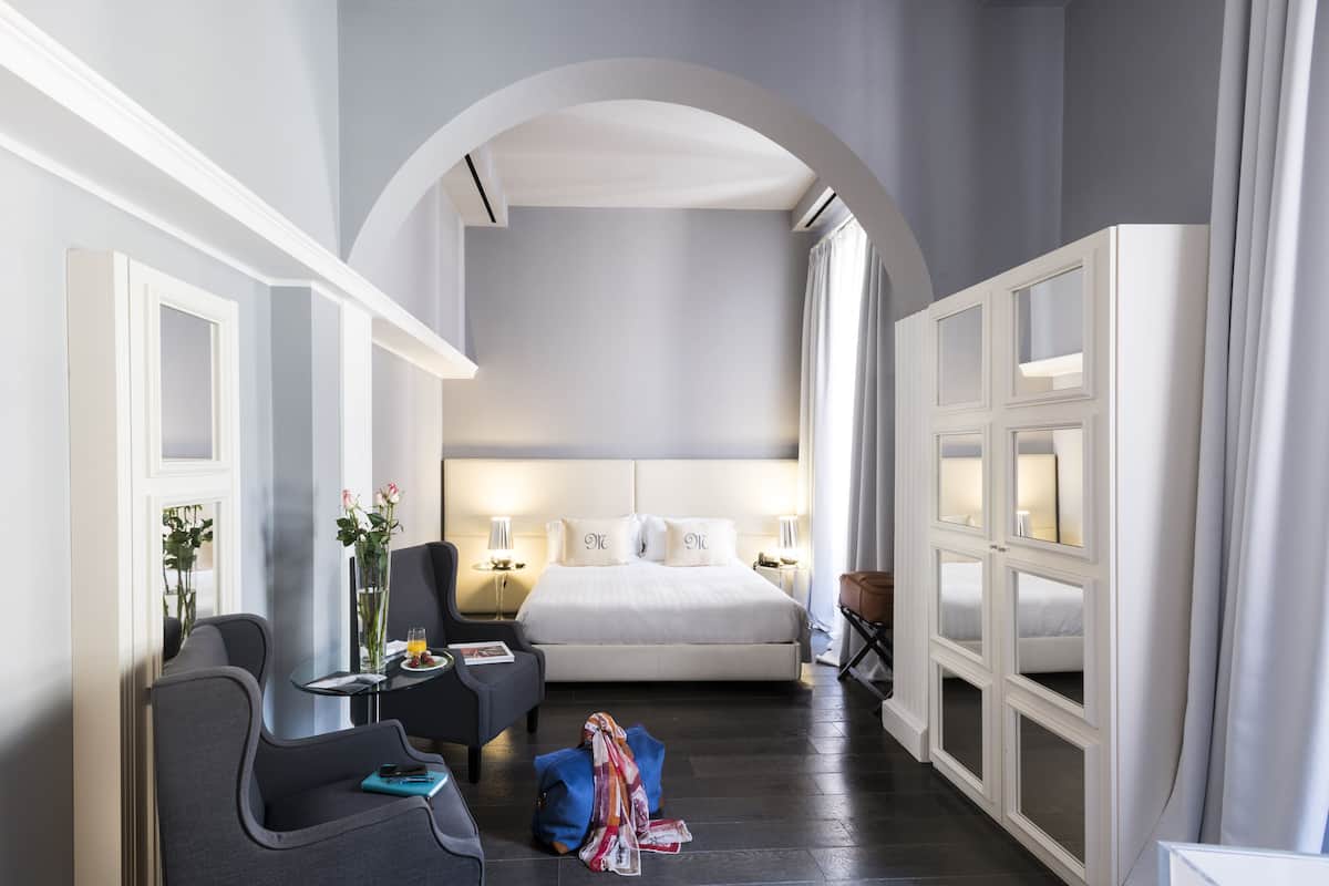 A hotel room with a large bed, a desk with a chair, a small table with a vase of flowers, and a wardrobe with mirrors.