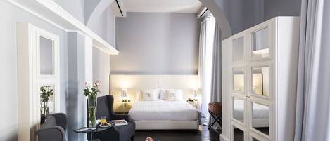 Habitación de hotel con una cama grande, un escritorio con silla, una mesita con un florero y un armario con espejos.
