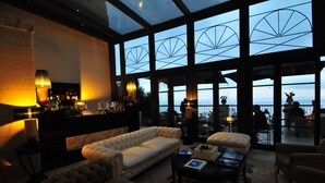 Un vaste espace salon comprenant un grand canapé, une table basse et un coin bar avec des bouteilles et des verres.