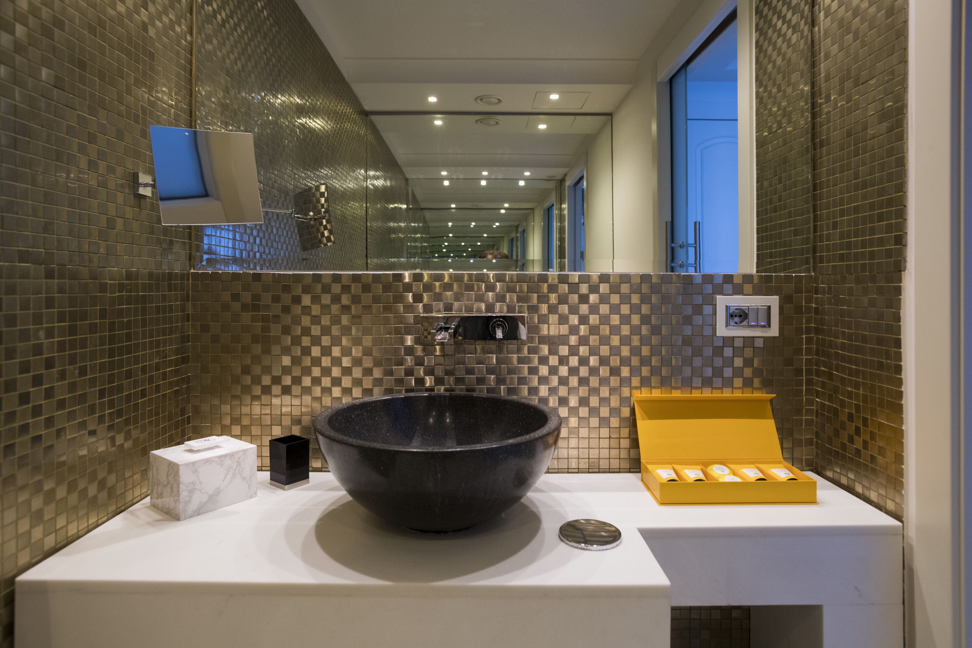 A modern bathroom with a large black basin, a white marble box, and a yellow soap dish.