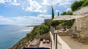 Un espace aménagé au bord de la piscine, avec des chaises longues et une vue sur la mer.
