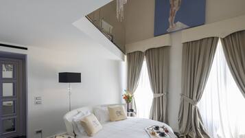 A modern hotel room with a large bed, a flat-screen TV, a small table with a tray of breakfast items, and a view of the city through large windows.