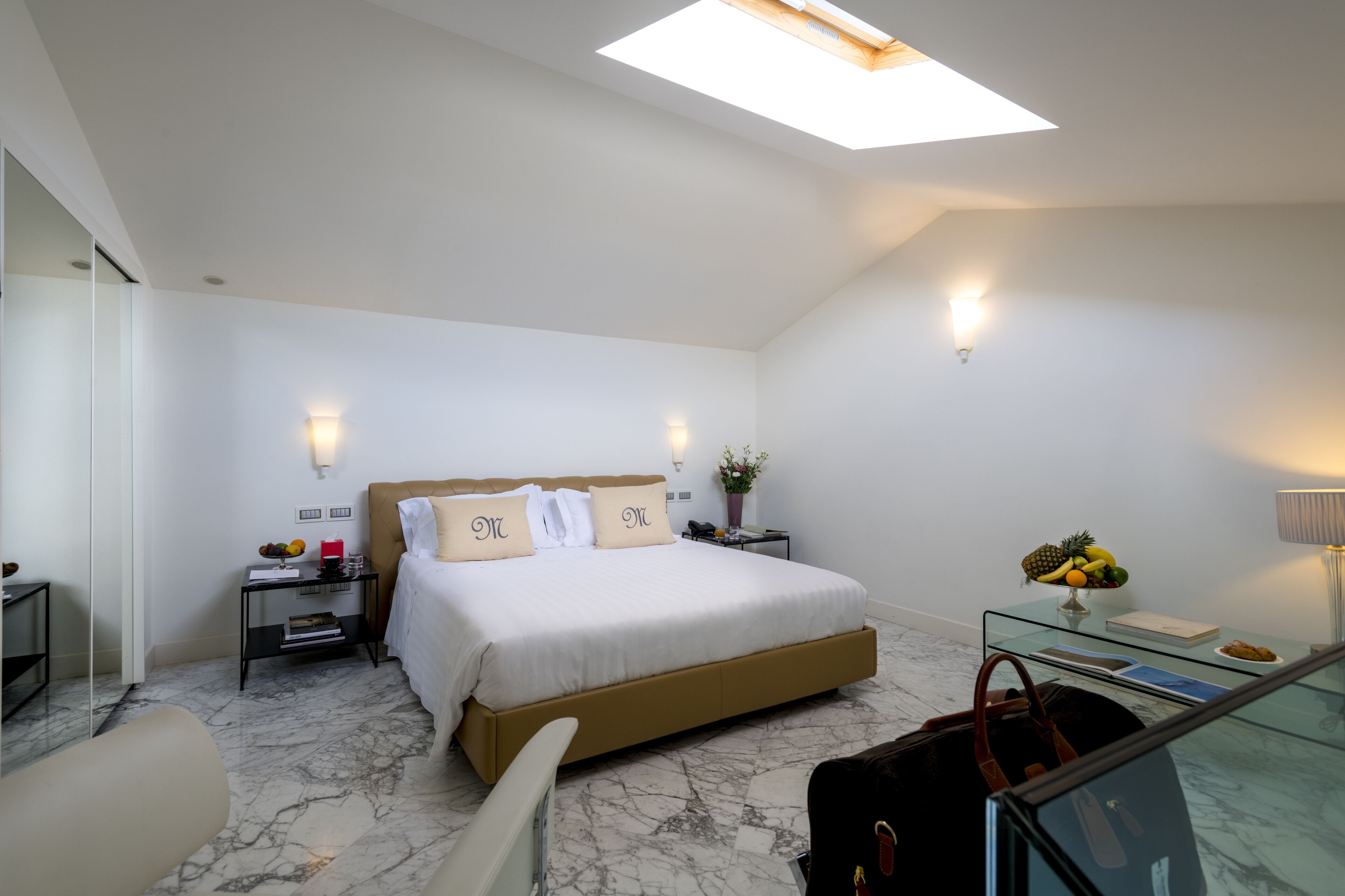 Una habitación de hotel moderna con una cama grande, una mesita de vidrio, una mesita de noche, un espejo y una lámpara en el techo.