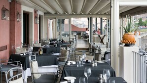 Un espace de restauration en plein air avec des tables prévues pour deux personnes, doté de chaises en métal et recouvert d’une nappe noire.