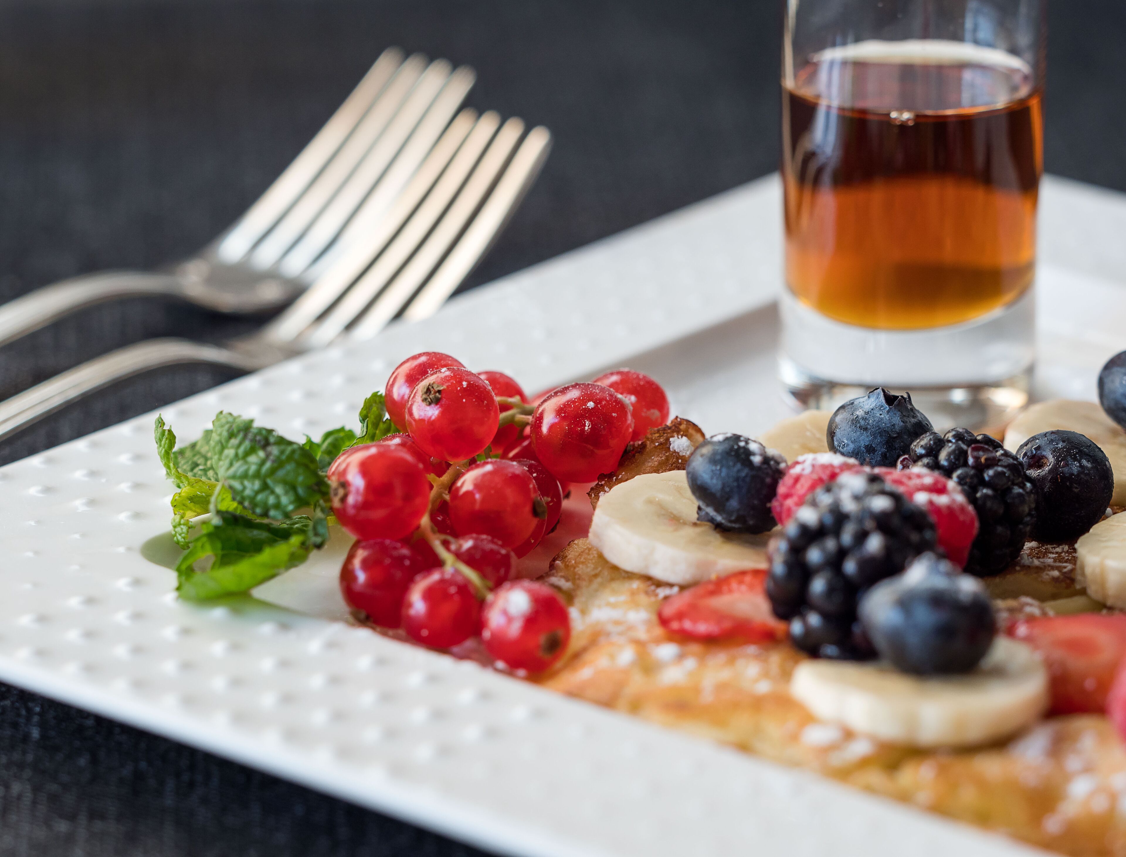 Une assiette de petit-déjeuner garnie de groseilles rouges, de myrtilles, de mûres et de tranches de banane.