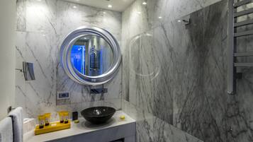 Un baño moderno con pared de mármol, espejo redondo, lavabo tipo cuenco negro y un perchero para toallas.