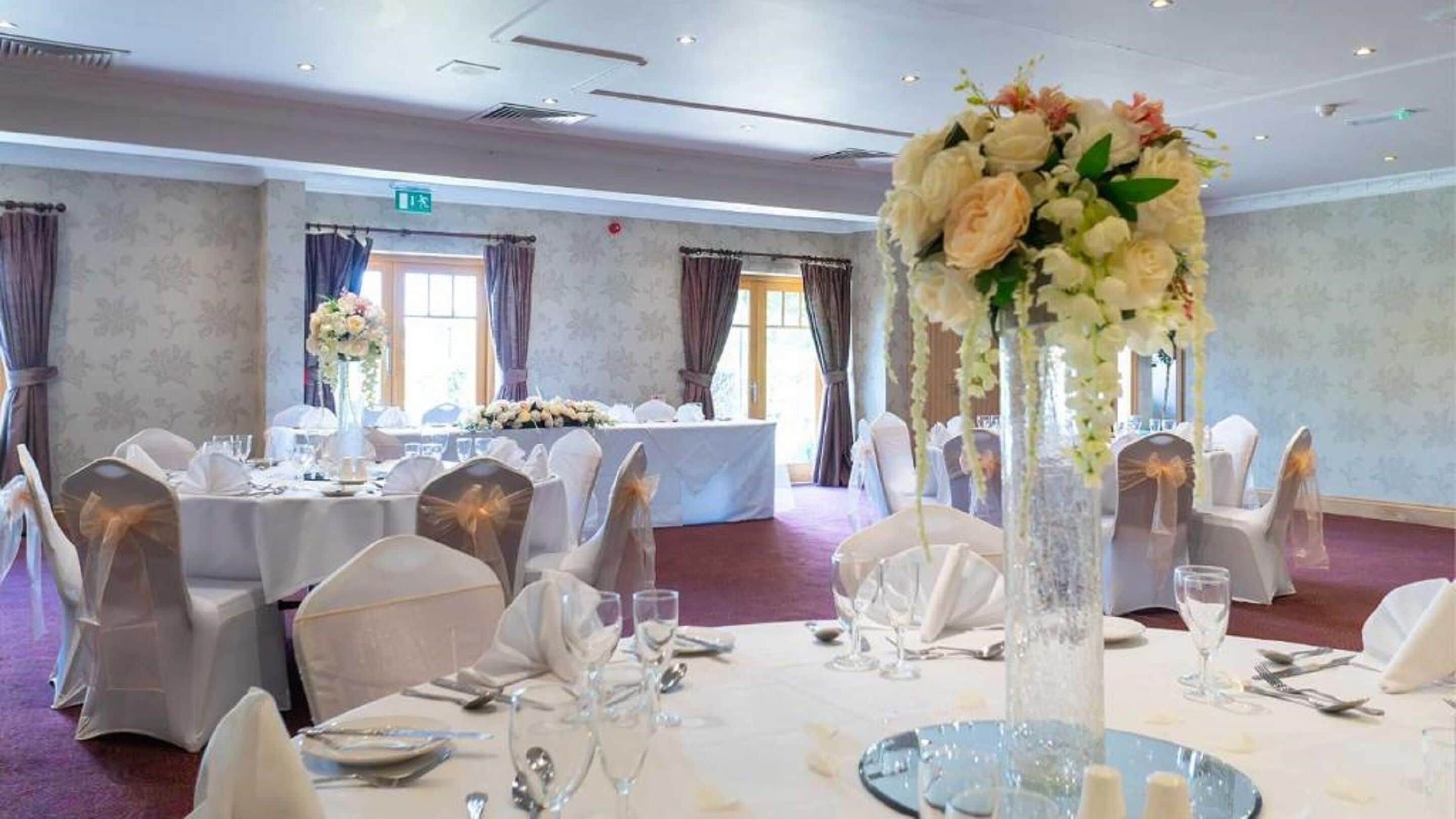 Une salle de banquet avec des tables rondes, des nappes blanches et des centres de table floraux.
