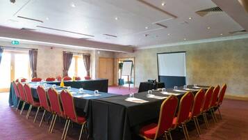 A conference room with a long table, red chairs, a projector screen, and a whiteboard.