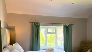 Habitació d'hotel amb un llit gran, una cadira, una finestra amb cortines i una làmpada.