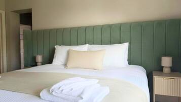 A neatly made bed with white linens, a green upholstered headboard, and a bedside table with a lamp.