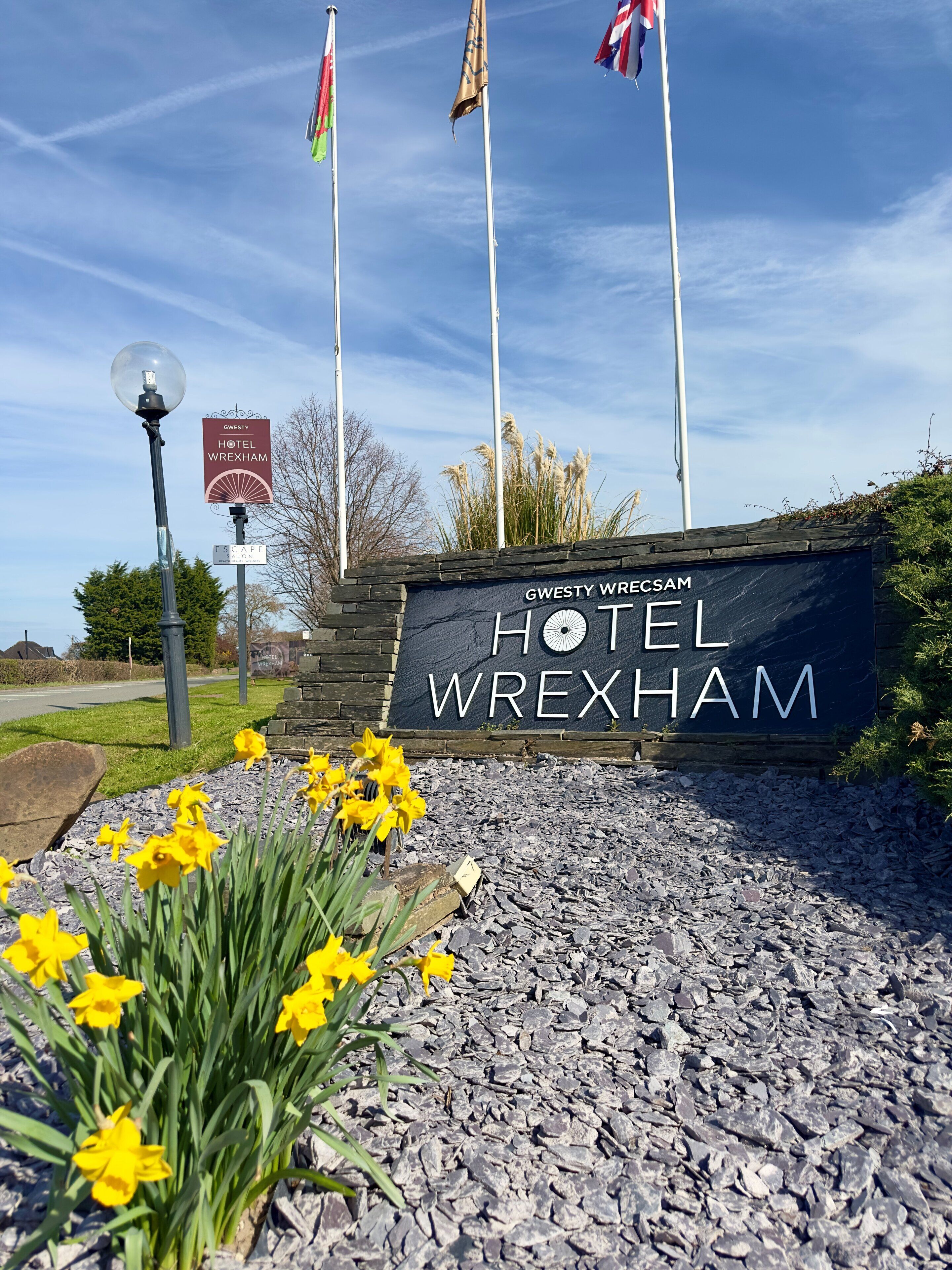A hotel sign with flags, a lamp post, and daffodils in the foreground.
