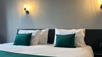 A hotel room with a bed, green and white bedding, two wall-mounted light fixtures, and a dark headboard.