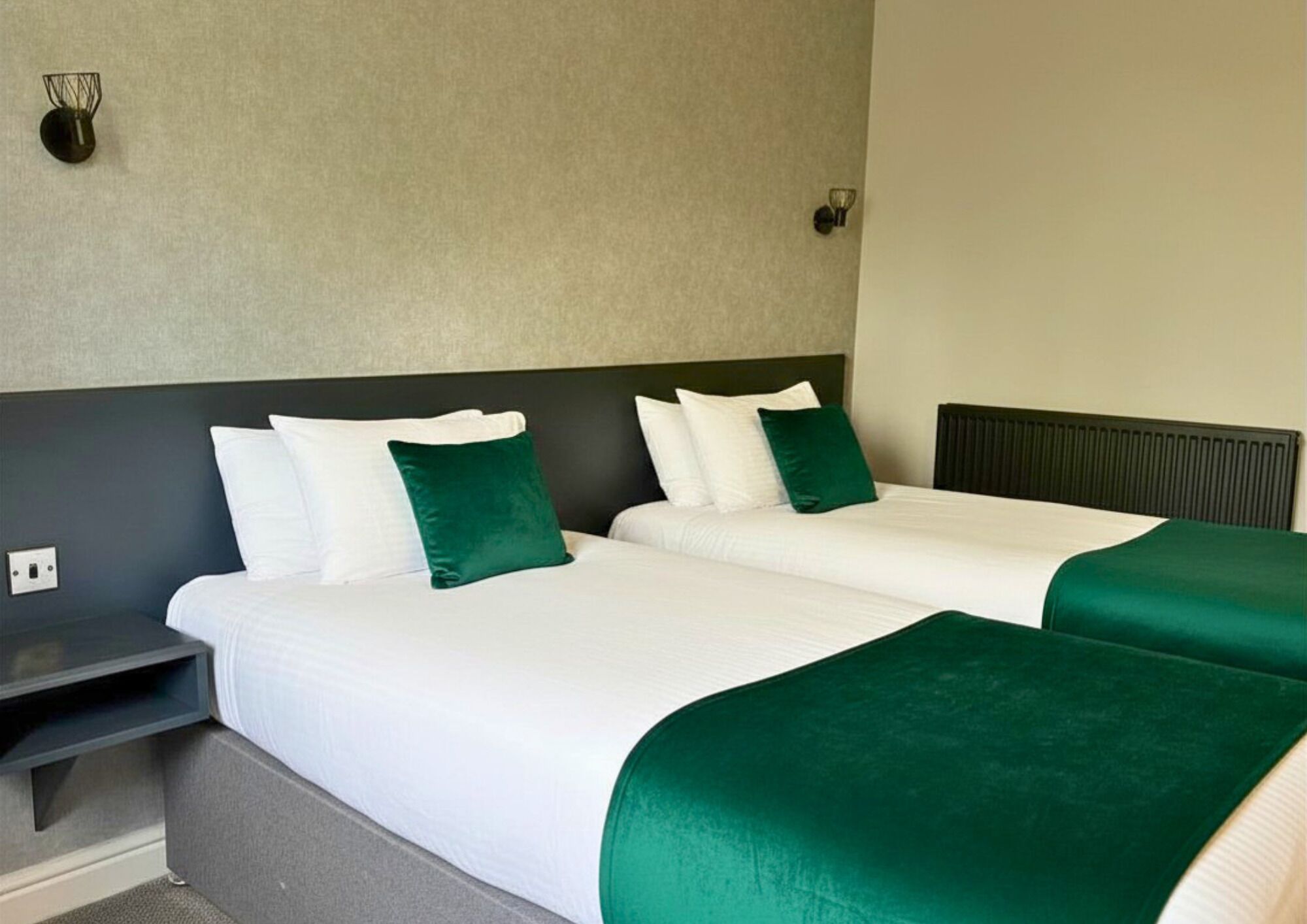 A hotel room with two beds, a nightstand, and a wall-mounted light fixture.