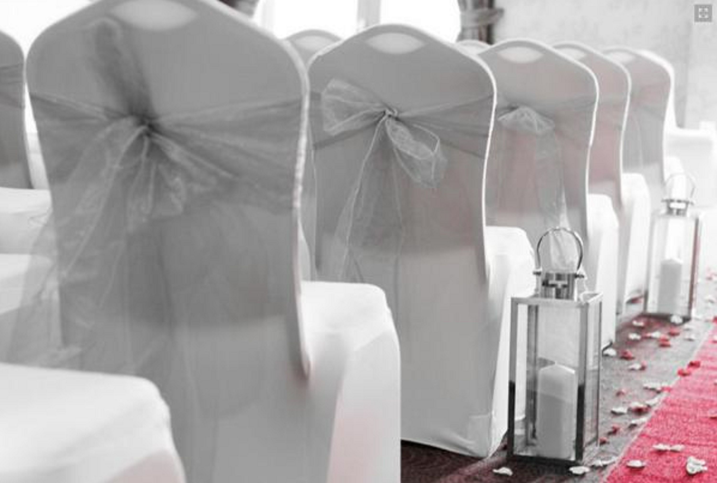 Rows of white chairs with sheer covers and bows, a red carpet with rose petals, and a clear glass lantern.