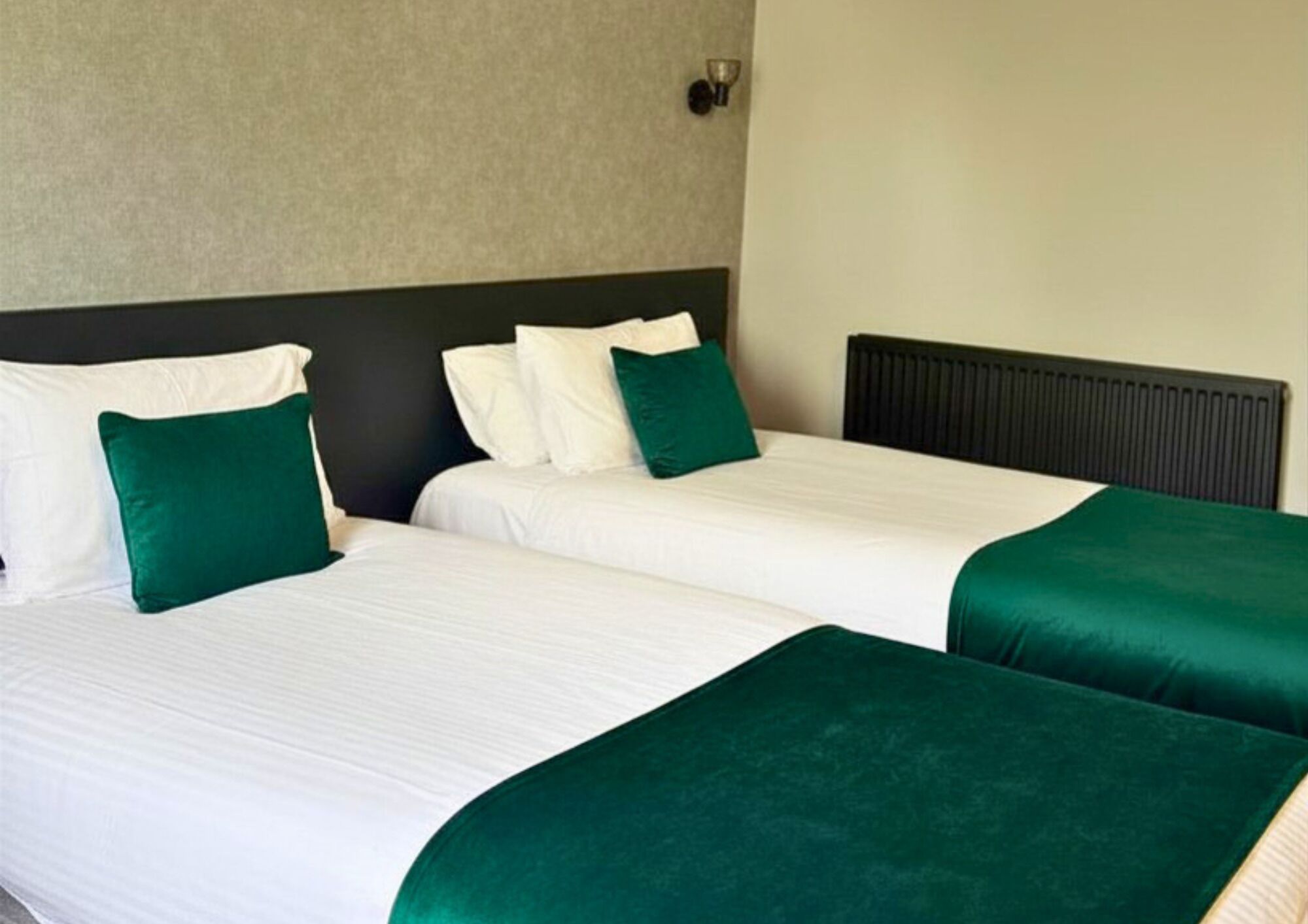 Habitación de hotel con dos camas, cada una con sábanas blancas y almohadones verdes.