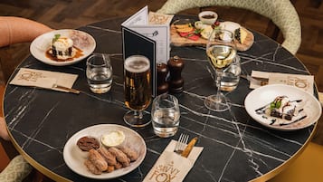 Una mesa redonda con tapa de mármol negro, rodeada de sillas. Hay platos de comida, copas de vino y un menú.
