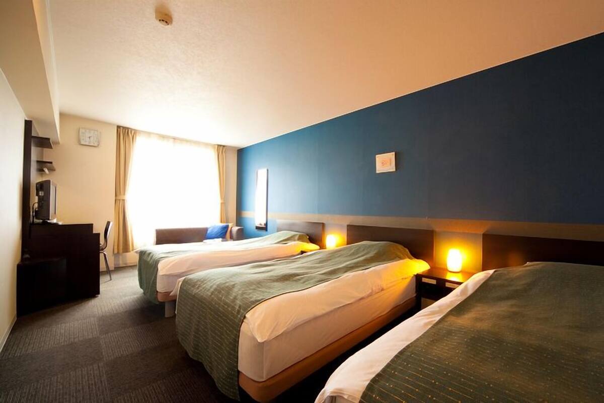 A hotel room with two beds, a desk, a chair, and a television.