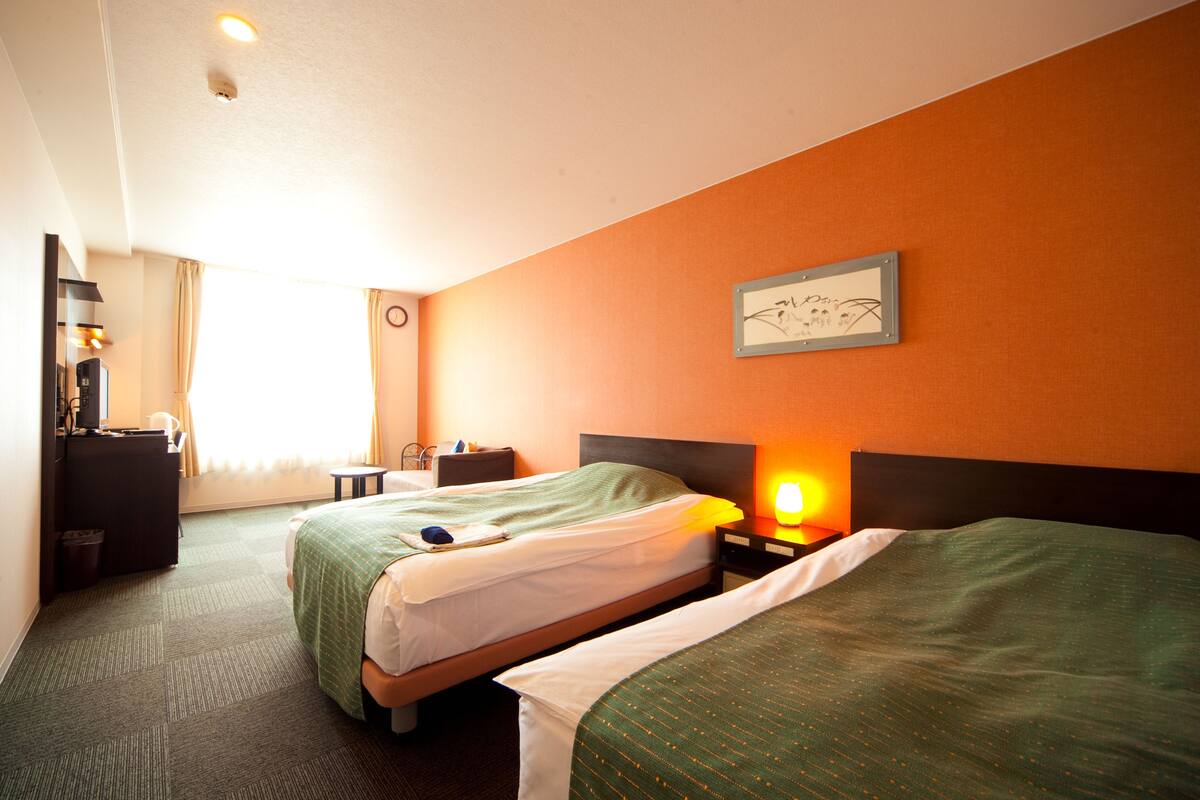 A hotel room with two beds, a desk, a chair, a lamp, and a framed picture on the wall.