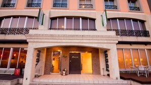 A hotel entrance with a dark door, a small outdoor seating area, and a potted plant.