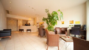 A hotel lobby with wicker furniture, a reception desk, and a large plant.