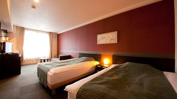 A hotel room with two beds, a desk with a computer, a small table, and a wall-mounted artwork.