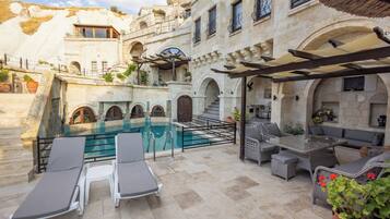 Zona junto a la piscina con sillones de descanso, una pérgola y un edificio de piedra con arcos.