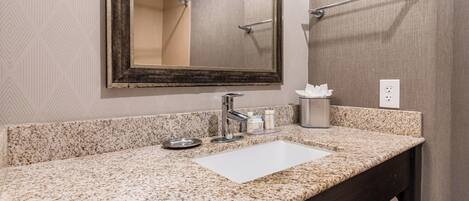 Une salle de bain avec un comptoir en granit, un lavabo blanc, un grand miroir et un porte-serviettes.