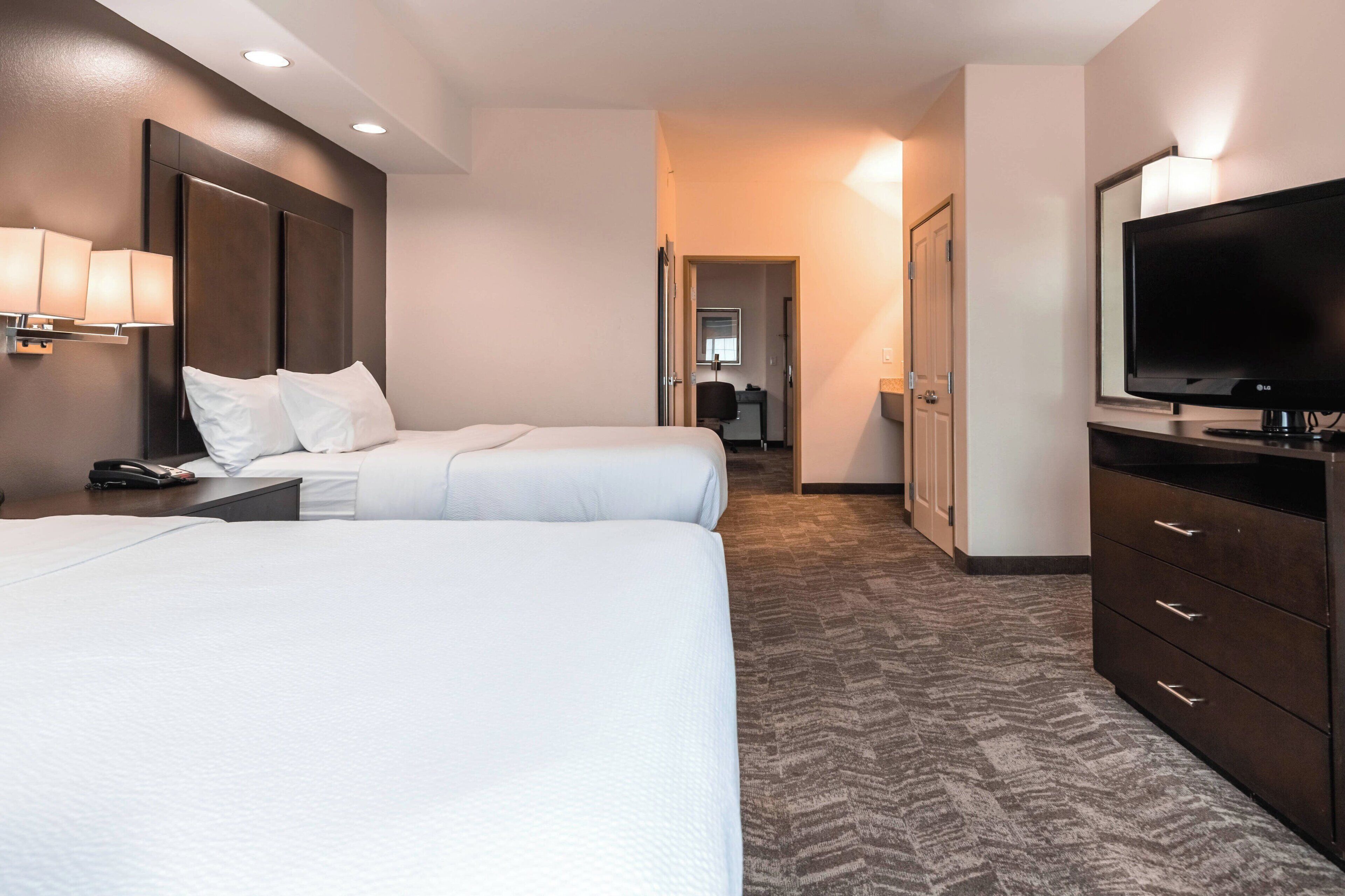 Hotellihuone, jossa on kaksi sänkyä, televisio, työpöytä lampun kanssa ja vaatekaappi.