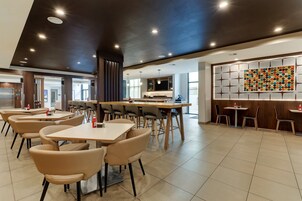 A modern dining area with multiple tables and chairs, a bar area, and a large decorative wall.