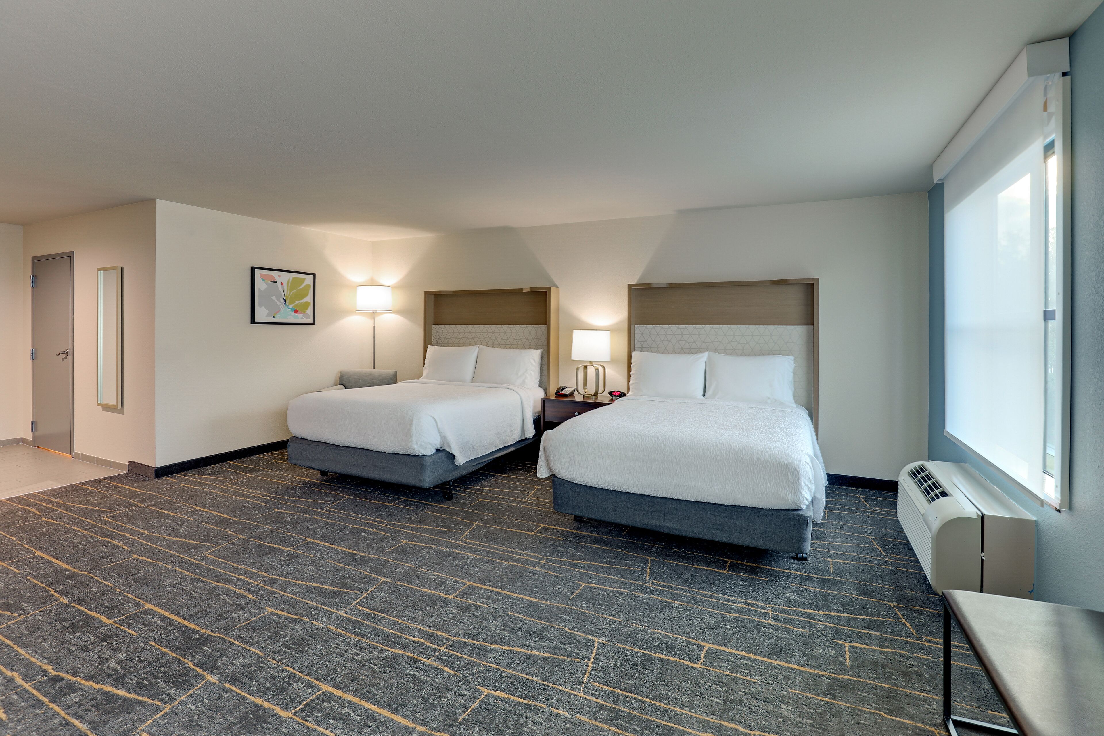 Habitación de hotel con dos camas, un ventanal grande y piso alfombrado.