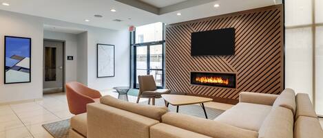 A modern living room with a beige sectional sofa, a flat-screen TV mounted on a wooden wall, and a fireplace.
