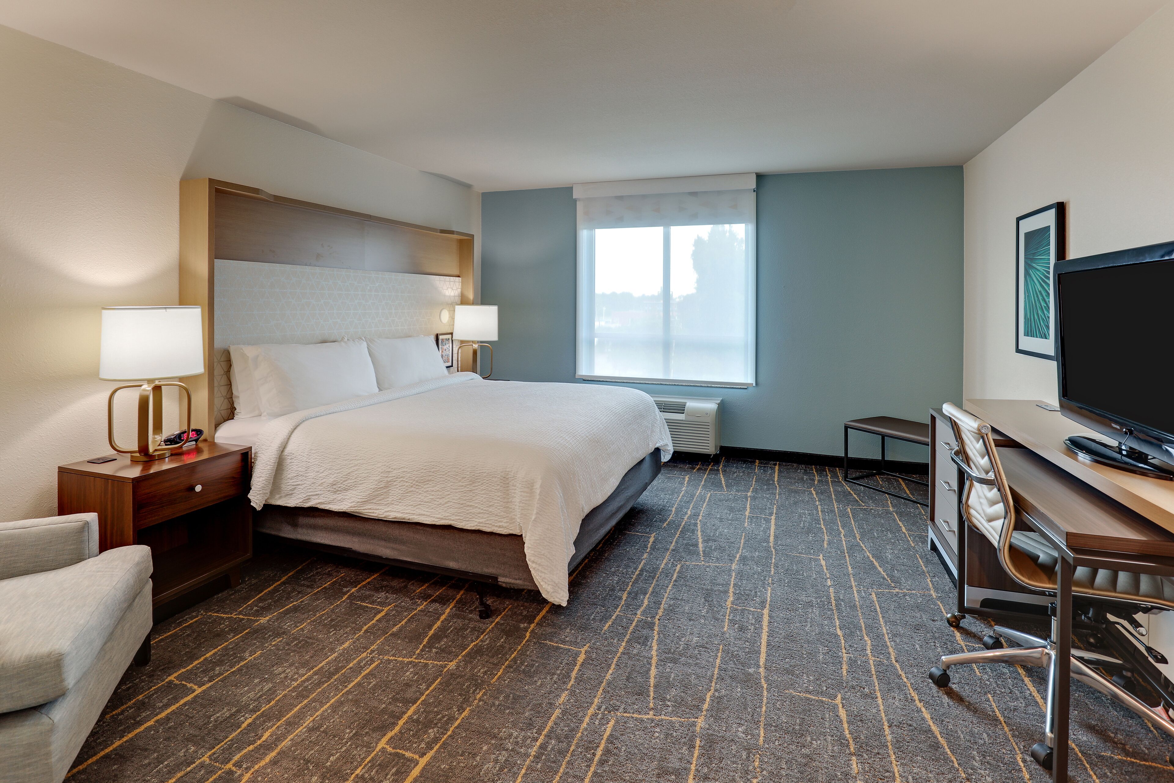A hotel room with a bed, bedside tables, a desk, a chair, a TV, and a window with a view.