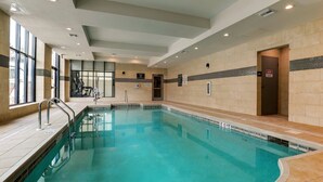 En stor inomhuspool med kristallklart blått vatten, omgiven av beige kakelväggar och ett kaklat golv.
