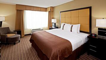 Una habitación de hotel con una cama grande, un escritorio con lámpara, una silla, una ventana con cortinas y un reloj de pared.