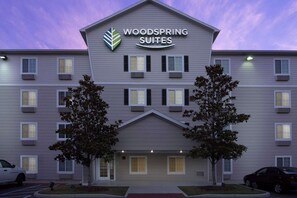 A multi-story hotel with a sign reading "Woodspring Suites." There are trees in front of the building, and a parking lot with cars. - WoodSpring Suites Gainesville I-75 (Gainesville)